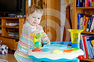 Happy joyful baby girl playing with different colorful toys at home. Adorable healthy toddler child having fun with