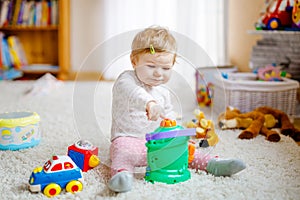 Happy joyful baby girl playing with different colorful toys at home. Adorable healthy toddler child having fun with