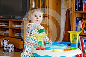 Happy joyful baby girl playing with different colorful toys at home. Adorable healthy toddler child having fun with