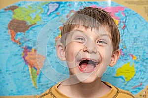 Happy and joyful boy on the background of the atlas of the world, a schoolboy studying science