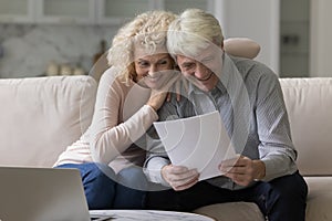 Happy joyful elder retired couple sitting close on couch