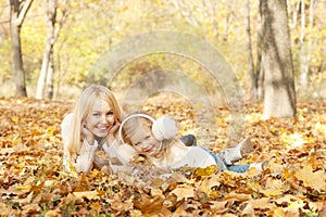 Happy joyful family portrait, blonde mother and blonde daughter have a rest laying outdoor in autumn park