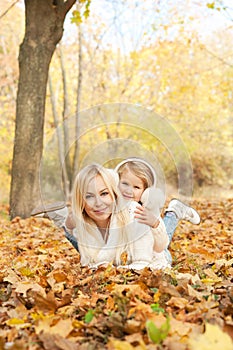 Happy joyful family portrait, blonde mother and blonde daughter laying outdoor in autumn park