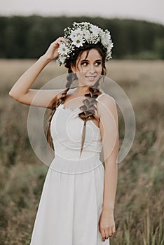 Happy joyful girl with braids and a flower wreath in a white dress smiles