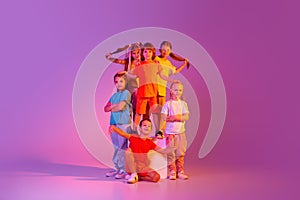 Happy, joyful kids, school age girls and boys in bright clothes posing isolated on pink background in neon. Concept of