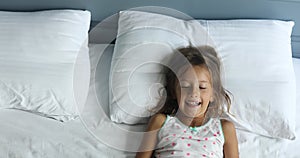 Happy, joyful Little girl wakes up from sleep and make faces, dapples on a big and cozy bed
