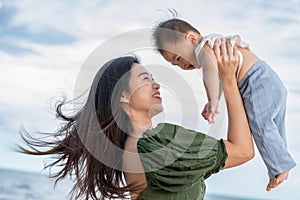 Happy Joyful mother and Son having fun Playing on the Beach together. Asian mom walks by ocean on the beach and throwing up her