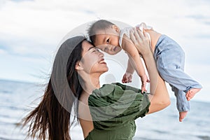 Happy Joyful mother and Son having fun Playing on the Beach together. Asian mom walks by ocean on the beach and throwing up her