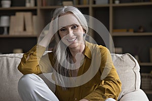 Happy joyful older 50s woman sitting on couch at home