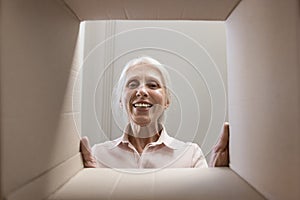 Happy joyful senior woman looking at camera through cardboard box