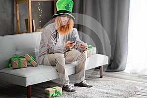 Happy joyful shopper guy in leprechaun hat buying St.Patricks day gifts online, using smartphone, credit card, paying on