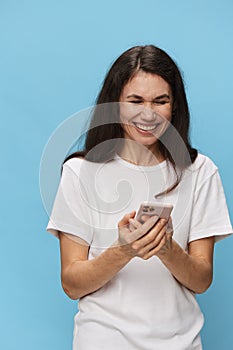 a happy, joyful woman with beautiful long hair, in a light T-shirt, stands with a fashionable phone in her hands and