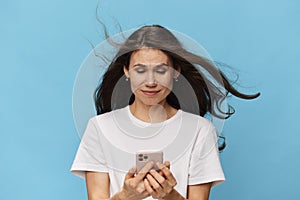 a happy, joyful woman with beautiful long hair, in a light T-shirt, stands with a fashionable phone in her hands