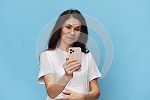 A happy, joyful woman with beautiful long hair, in a light t-shirt, stands with a fashionable phone in her hands and