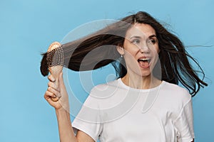 happy, joyful woman combing her long, beautiful, well-groomed hair with a wooden comb in a white t-shirt on a light blue