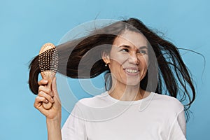 happy, joyful woman combing her long, beautiful, well-groomed hair with a wooden comb in a white t-shirt on a light blue