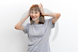 a happy, joyful woman in a gray cotton T-shirt stands against a light background, smiling happily and looking away