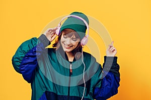 a happy, joyful woman in a green jacket and hat enjoys music standing in pink headphones on a yellow background