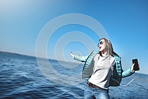 Happy joyful woman listening to music while being outdoor. Teenage female wearing headphones having fun on a walks near the sea
