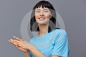 a happy, joyful woman smiles broadly with her teeth, standing on a gray background in a blue cotton T-shirt and looking