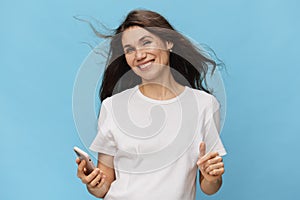 a happy, joyful woman stands with a phone in her hands spreading her arms to the sides. Horizontal photo on a light blue