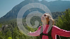 Happy joyful woman tourist enjoys breathing fresh air in mountains at sunny day. female hiker raising hands at amazing