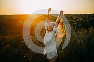 Happy joyful woman is walking on meadow at sunset