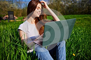 happy, joyful woman working on a laptop while sitting in a field