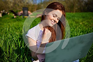 happy, joyful woman working on a laptop while sitting in a field