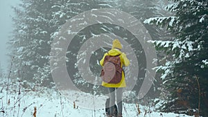 Happy joyful woman in yellow warm clothing invites to follow her at winter forest with falling snow. Outdoor Christmas