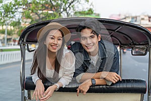 Happy and joyful Young Asian couple traveler tourists riding a tuk tuk tour, rickshaw style transportation on the street