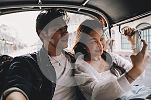 Happy and joyful Young Asian couple traveler tourists riding a tuk tuk tour, rickshaw style transportation on the street