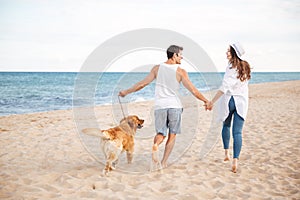 Happy joyful young couple running on beach with their dog