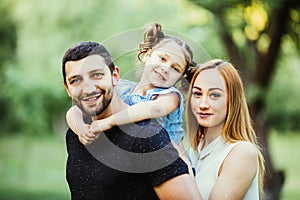 Happy joyful young family father, mother and little daughter having fun outdoors, playing together in summer park, countryside.