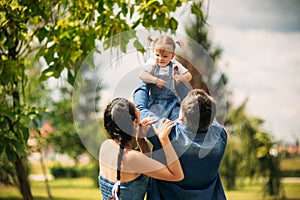 Happy joyful young family father, mother and little daughter having fun outdoors, playing together in summer park