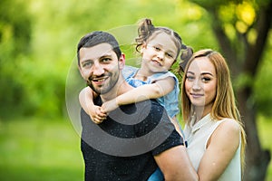 Happy joyful young family father, mother and little daughter having fun outdoors, playing together in summer park, countryside.