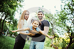 Happy joyful young family father, mother and little daughter having fun outdoors, playing together in summer park. Daughter raided