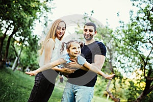 Happy joyful young family father, mother and little daughter having fun outdoors, playing together in summer park. Daughter raided