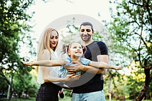 Happy joyful young family father, mother and little daughter having fun outdoors, playing together in summer park. Daughter raided