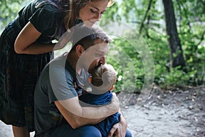 Happy joyful young family father, mother and little son hugging and kissing outdoors, playing together in summer park