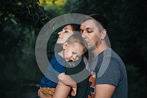 Happy joyful young family father, mother and little son outdoors, hugging together in summer park