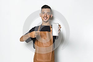 Happy joyful young man barista bartender or waitress demonstrating mobile cell phone on white background