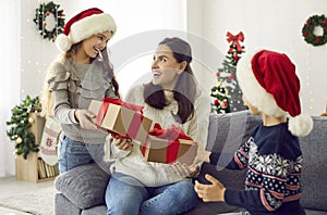 Happy joyful young mother gets unexpected presents from her loving children on Xmas Day.