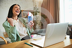 Happy, joyful young woman, employee sitting in office with laptop, holding plane tickets and showing excitement about