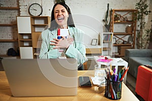 Happy, joyful young woman, employee sitting in office with laptop, holding plane tickets and showing excitement about