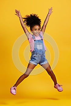 Happy, jump and child hands raised jumping in happiness, joy and smile while isolated in a studio yellow background