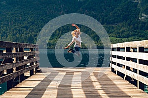 The happy jump, female, girl, woman stand on wooden pier. Mountain lake landscape, Green forest, sunset time. travel and vacation