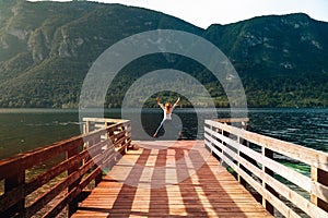 The happy jump, female, girl, woman on wooden pier. Mountain lake landscape, Green forest, sunset time. travel and vacation
