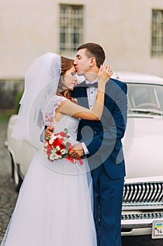 Happy just married couple holding each other in the background of vintage car