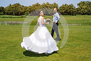 Happy just married young wedding couple having fun in the park. Bride and groom together, love and marriage theme.